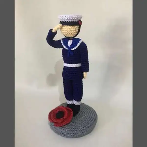 Pilot amigurumi with blue-grey uniform standing on platform next to poppy detail and LED light