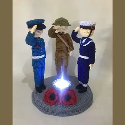 Three uniformed amigurumi figures on a round platform with LED centrepiece and poppies, handmade crochet display amigurumi