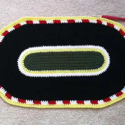 Finished oval race track crochet mat with green outer border and black track area amigurumi-style display