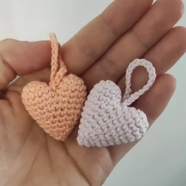 two small crocheted heart halves in progress on a hook demonstrating starting rounds and shaping