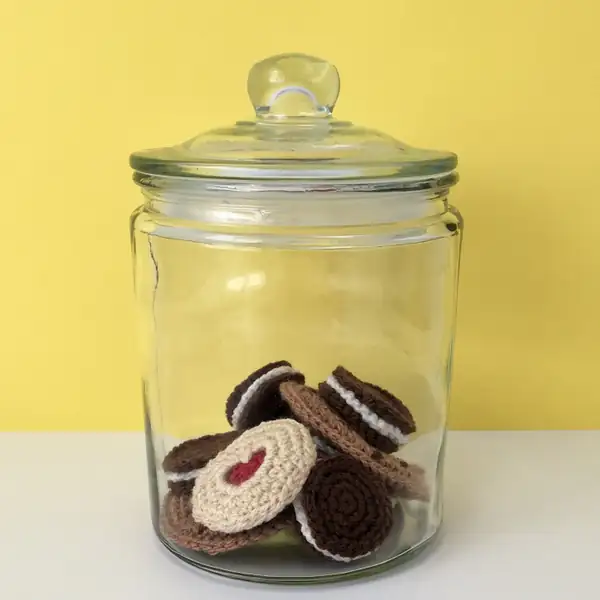 three small crochet biscuits arranged on a plate: Choc Chip, Jammie Dodger and Oreo amigurumi
