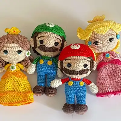 Four finished Mario Bros amigurumi characters including Mario, Luigi and two princesses arranged together showcasing caps, overalls and dresses