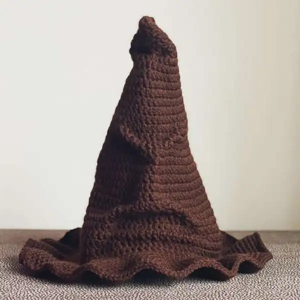 Materials laid out for the Sorting Hat project including brown chenille yarn, a Size N crochet hook, yarn needle and felt pieces