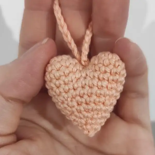 closeup of a crocheted heart being held to show side profile and stuffing before closing the seam