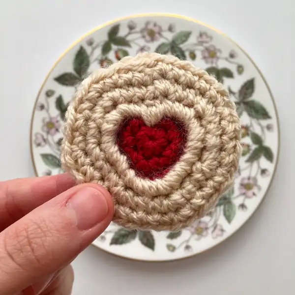 single Jammie Dodger crochet biscuit with a red heart centre on a floral plate