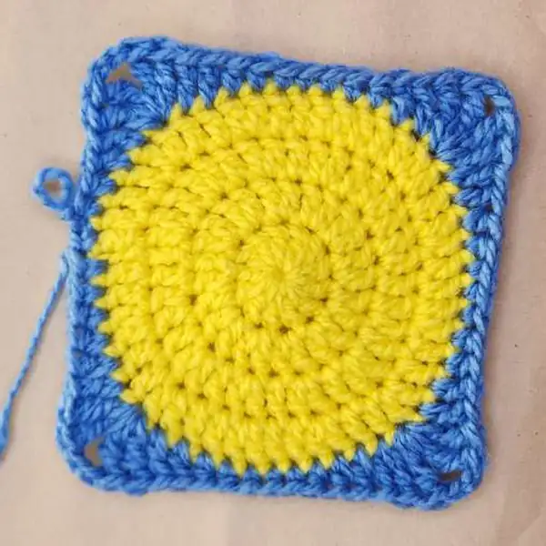 Finished fish granny square displayed on blue base